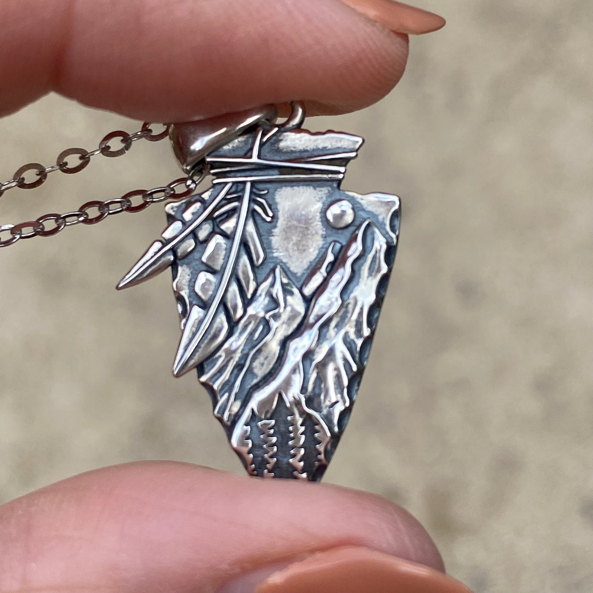 Miss Valkyrie arrowhead necklace sterling silver with intricate nature-inspired engravings held between fingers