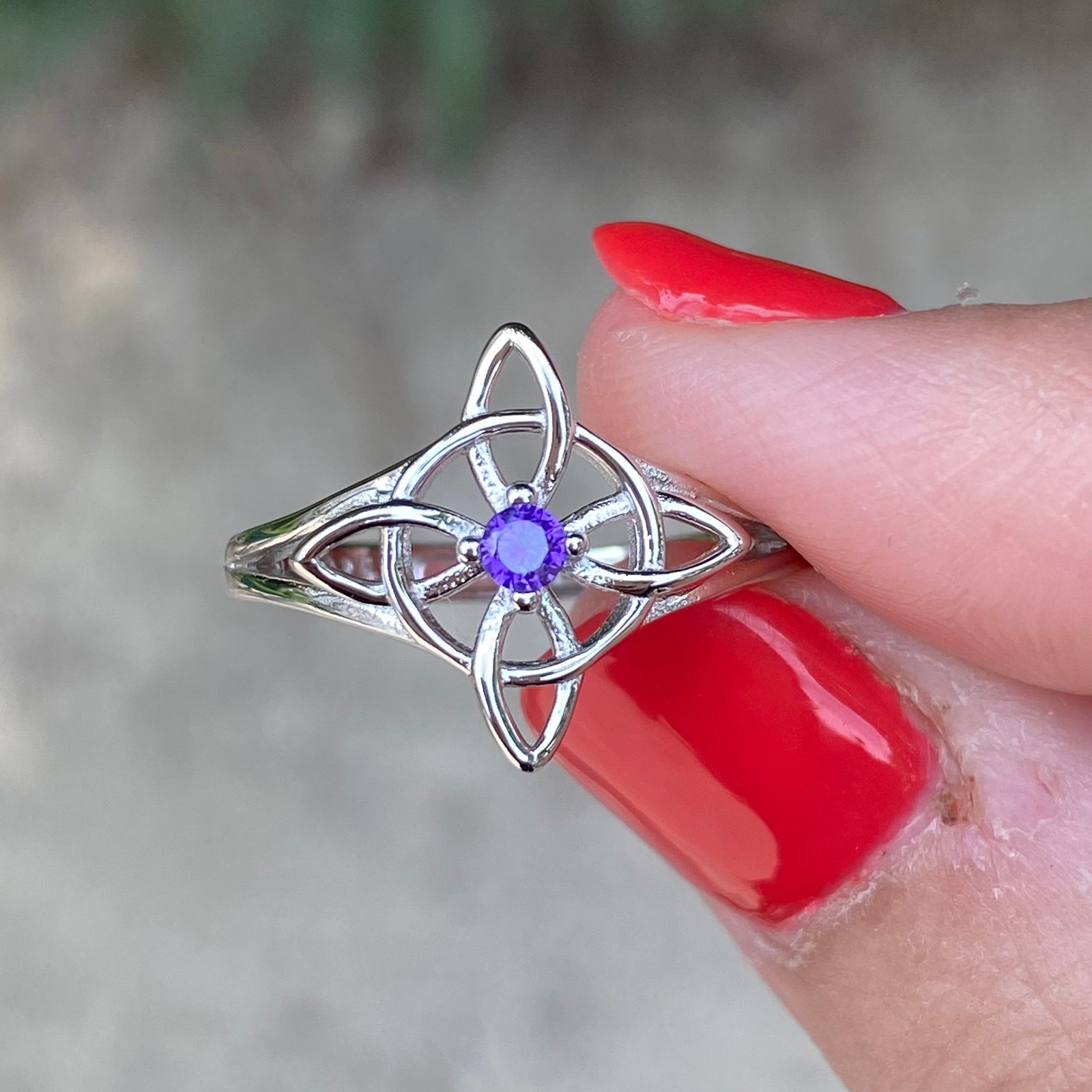 Sterling silver adjustable purple stone Witch knot ring held between fingers with red nail polish