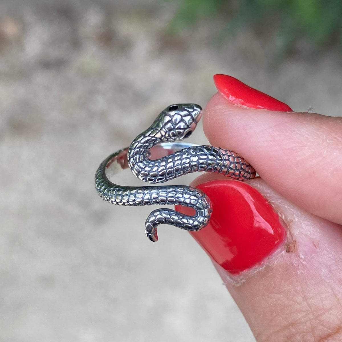 Sterling silver adjustable snake ring with detailed scales held between fingers with red nail polish