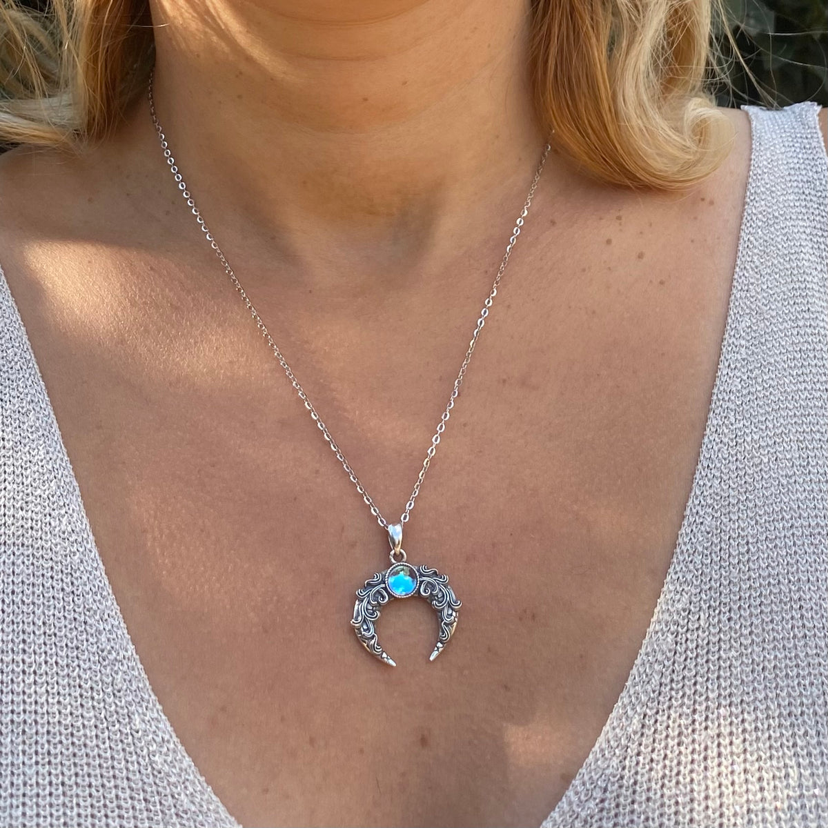 Sterling silver blue moon crescent necklace with intricate design and blue gemstone pendant worn on neck