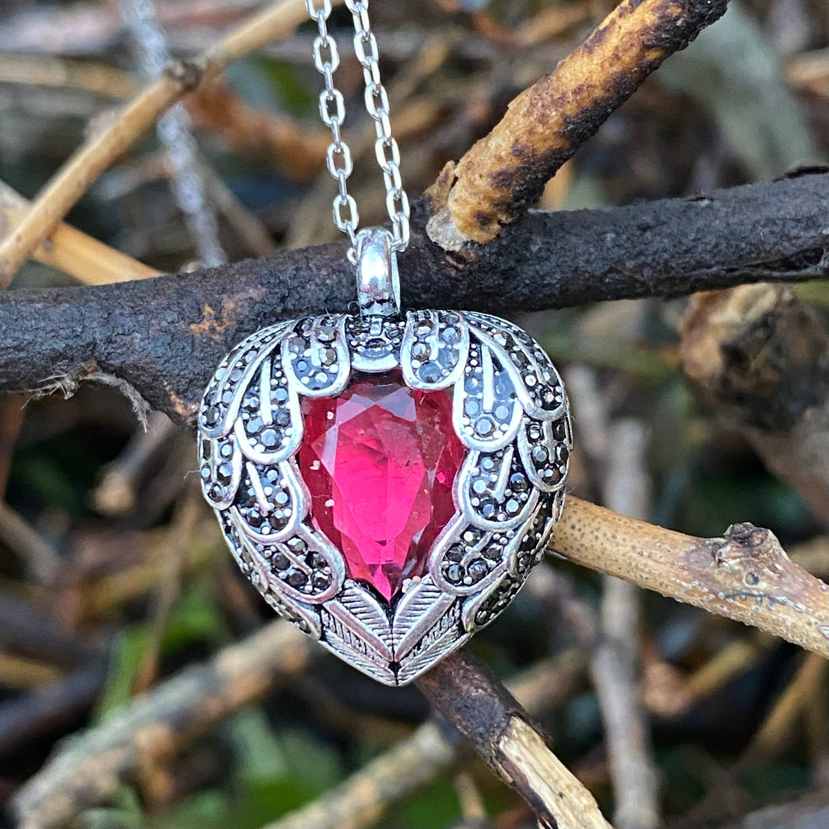 Sterling silver heart wing necklace with a red gemstone pendant hanging on a chain