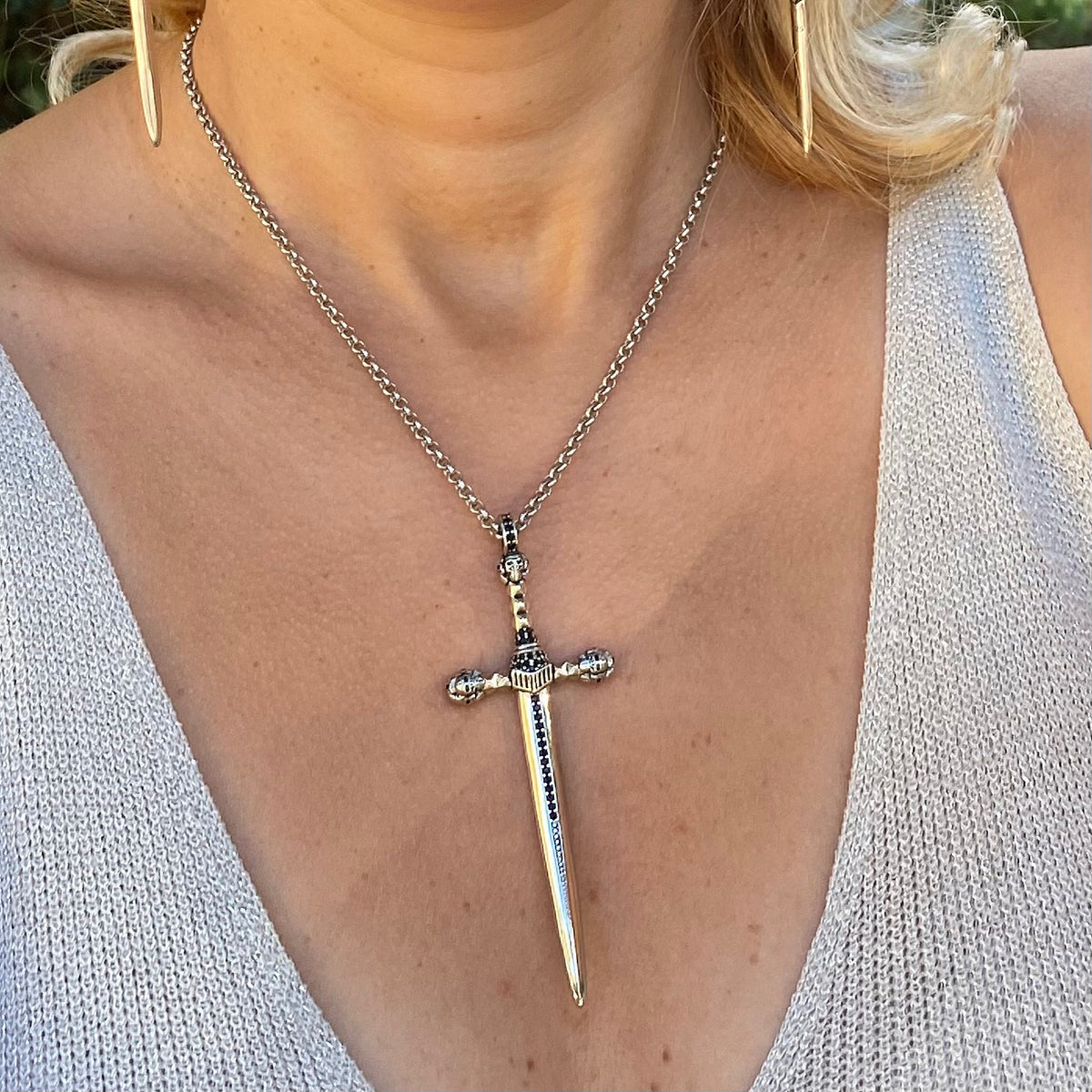 Sterling silver sword necklace worn on a woman with a light gray knit top and gold earrings