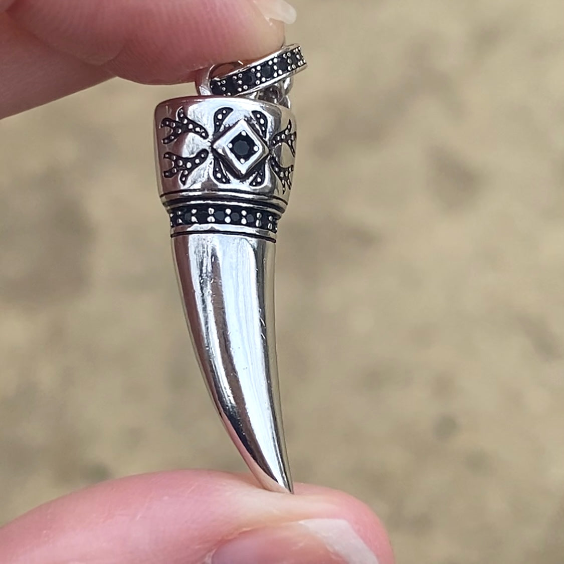 Sterling silver wolf tooth necklace pendant with intricate tribal engravings held between fingers