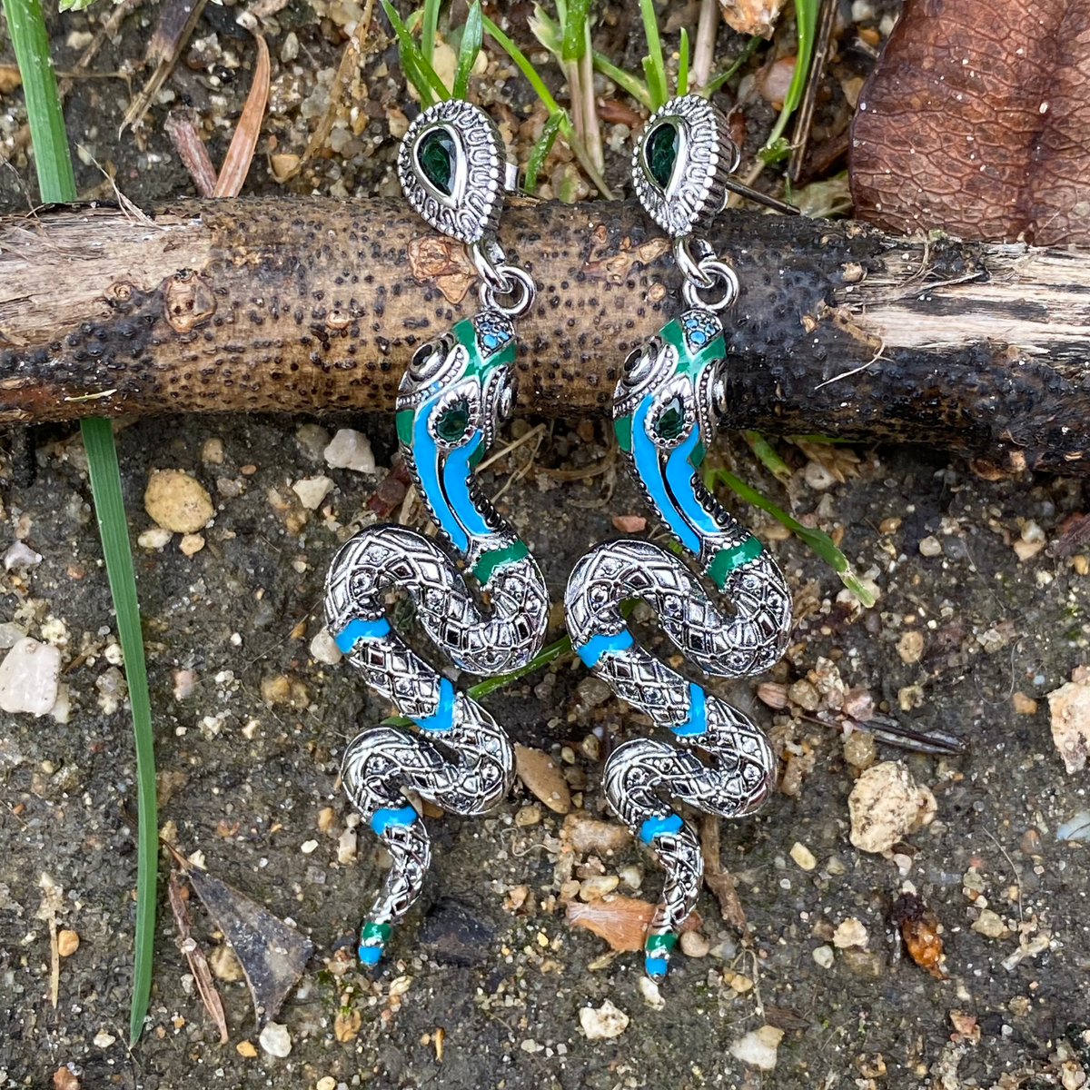 Sterling silver Snake earrings with blue and green enamel detailing by Miss Valkyrie displayed on natural ground